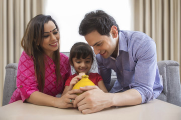 Parents and daughter saving money in clay piggy bank