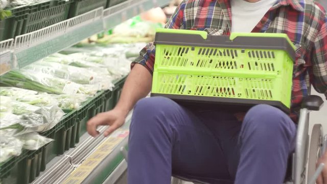 Man with a disability in a wheelchair shopping in the supermarket.He has a basket of food on his knees.Close up