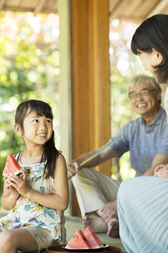 縁側でスイカを食べる女の子と祖父母