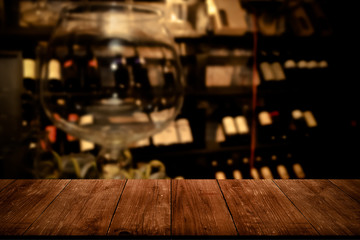 View from dark wooden table on a blurred kitchen with bottles of wine on shelves. Toned