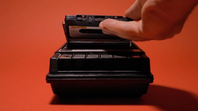 Inserting and removing an audio cassette from a retro vintage player. Medium shot on a red background.
