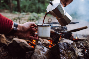 Making coffee process on the campfire. Man pour coffe in potter cup