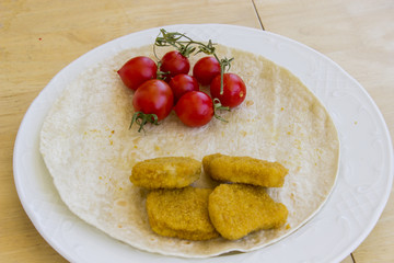 Beautiful shot of chicken nuggets and small red fresh tomatoes on the wide white plate as a breakfast with thin bread