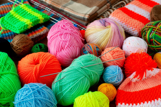 Many colorful balls of yarn for knitting. Multicolored yarn for knitting is gathered in a heap. Knitted clothes, knitting needles and yarn in the background of a plaid.