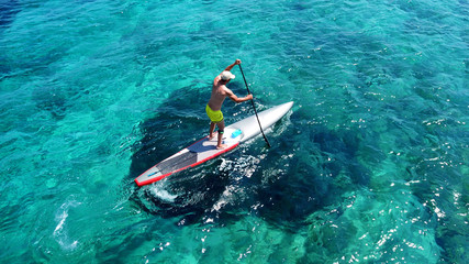 Aerial drone bird's eye view of fit man exercising sup board in turquoise tropical clear waters