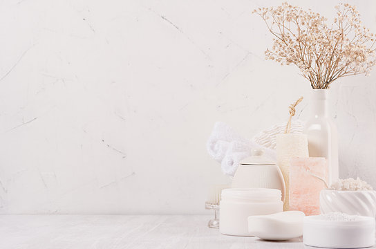 Natural spa cosmetics with white cream, clay, salt, soap and small dry flowers on white wood background, interior, border.