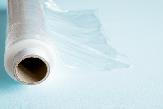 Roll of transparent polyethylene food film for packing products on the pastel blue table.