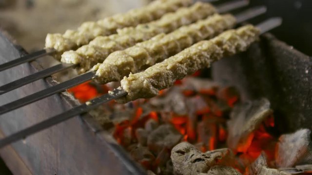 Close-up of putting metal skewers with lula kebab on hot grill with burning charcoal