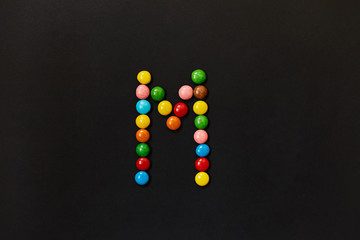English Alphabet made of colored candies. The letter M.