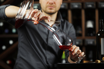 Sommelier pouring wine into glass from mixing bowl. Male waiter