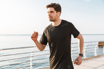 Handsome young sportsman running outdoors listening music