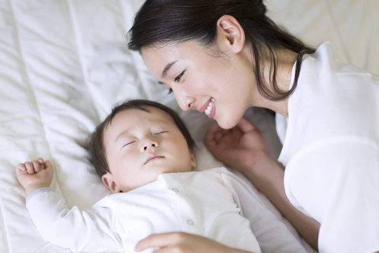 眠っている赤ちゃんを見て微笑む母親