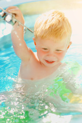 Fototapeta na wymiar Baby with toy plane in swimming pool. Little boy learning to swim in outdoor pool. Swimming with kids. Healthy sport activity for children. Sun protection swim wear. Water toys.