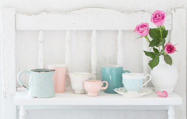 pinc roses in vase and dinnerware on white wooden shelf