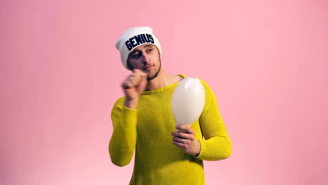 The guy in a yellow sweater and a white hat is imaginarily writing his hand holding the lamp in the other hand. Idea concept.
