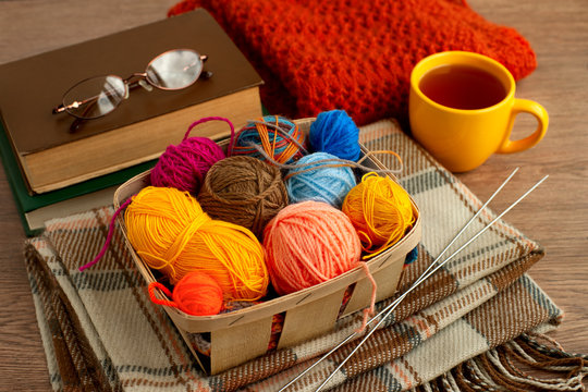 Yarn and knitting needles in a cozy atmosphere. Glasses, yarn, knitting needles, a book, tea, a shawl and a tippet for needlework in a warm home environment. Knitting and coziness.