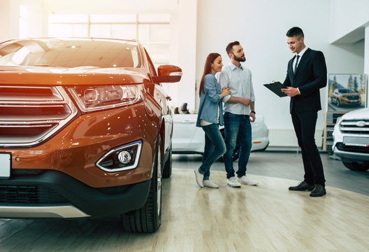 Young Modern Happy Couple Buying A New Car In City Dealership And Talking With Salesman