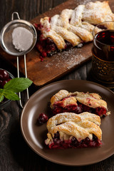 Homemade cherry puff pastry braid, on blue wooden background.