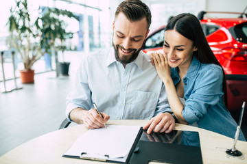 Signing of documents on the purchase of cars. Beautiful happy couple sitting at the table signing a...