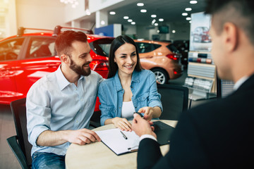 Husband bought his wife the first car. Happy married couple gets the keys from the seller in the dealership.