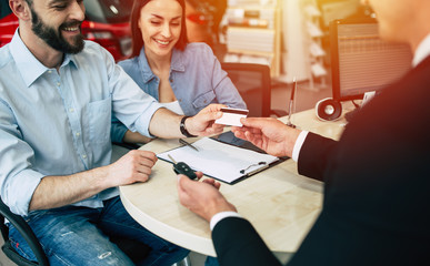 Young happy family buys a new car in the dealership with help of bank card.