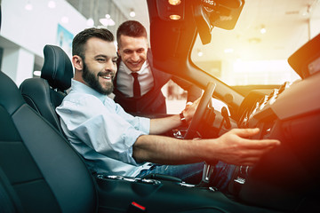 Very beautiful design. Handsome young bearded man buys and inspects a sports car in a dealership.