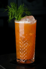 carrot cocktail with herbs in a glass of ice. Cocktail on a black background with bubbles