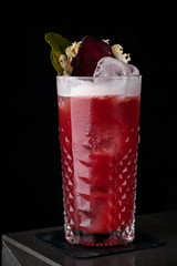 Red cocktail with foam, beet and mint in a cold glass on the bar in a black background