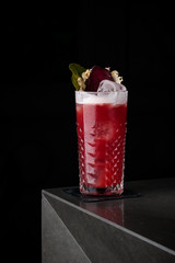 Red cocktail with foam, beet and mint in a cold glass on the bar in a black background