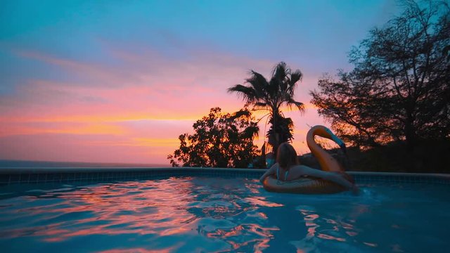 Girl on inflatable gold goose in pool during amazing sunset, Curacao