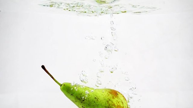 The green pear sinks into the water with bubbles and flips over there. Video recording of pear in slow motion.