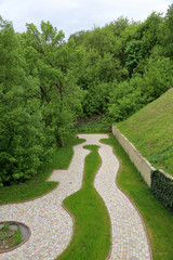 Fototapeta premium A winding path for walks from stone tiles among trees and a green lawn 