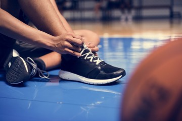African American teenage boy tying his shoe laces on a basketball court