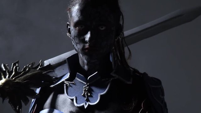 Pathos dark warrior with white eyes holds a large sword on her shoulder and stay in smoke, slow motion