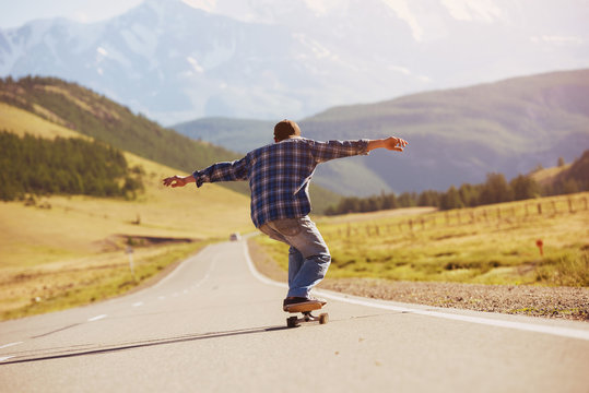 Man skating on longboard straight mountain road