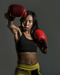 close up portrait of young fit Asian Chinese woman in fitness top and boxing gloves throwing punch...