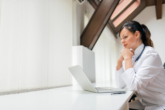 Pensive Doctor Looking At Laptop Screen In The Office. Copy Space.