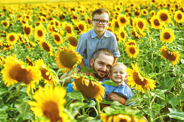 Cheerful father with his sons on vacation in the field with sunflowers . The parent plays with his son . Father's day