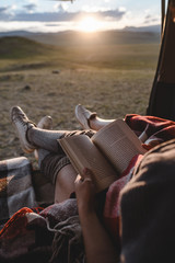 two young girls sitting in the van and reading a book. beautiful sunset in mountain valley on the background.