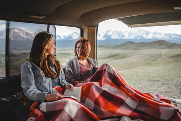 two young girls sitting in the van and talking with each other. beautiful mountain valley on the background. - 212744069