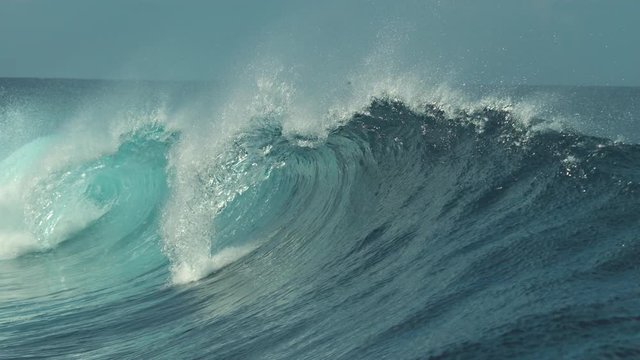 SLOW MOTION, CLOSE UP: Raging barrel wave glimmers in the bright summer sunshine in beautiful Tahiti. Spectacular glassy wave coming from the Pacific ocean breaks towards the coast of French Polynesia