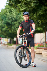 Young male bicyclist in cycling clothes and protective helmet standing near bike in empty city street. Sportsman shooting for sport ad clothing campaign. Concept of healthy lifestyle