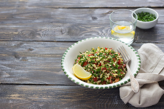 Tabbouleh, traditional arabic salad of bulgur, parsley and tomatoes on a wooden table with free space. Delicious diet food