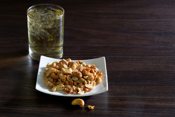 Cashew nut mix with salt in white dish and whisky in glass, All put on  brown wooden table