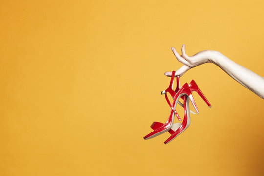Hand with high hell shoes in studio on yellow background
