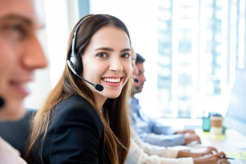 Smiling friendly woman working in call center office with team as the customer care operators