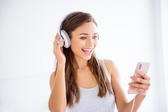 Head shot portrait of cheerful positive girl using smart phone and headset listening favorite music enjoying free time