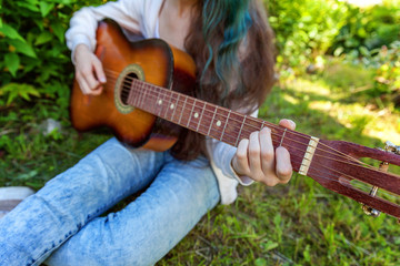 Closeup of woman hands playing acoustic guitar on park or garden background. Teen girl learning to...
