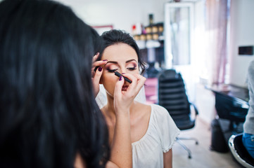 Makeup artist or beautician doing wedding makeup for a gorgeous young bride in a salon.