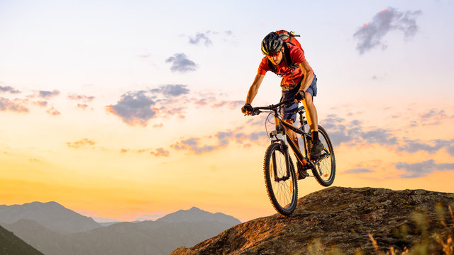 Cyclist in Red Riding the Bike Down the Rock at Sunset. Extreme Sport and Enduro Biking Concept.